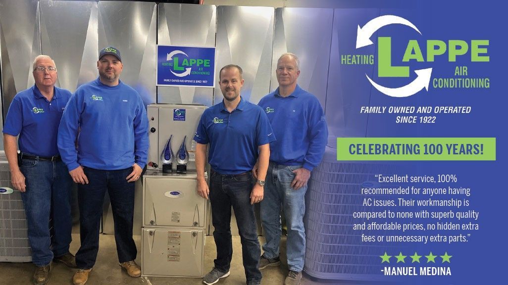 Four men in blue shirts pose with equipment, celebrating 100 years for
