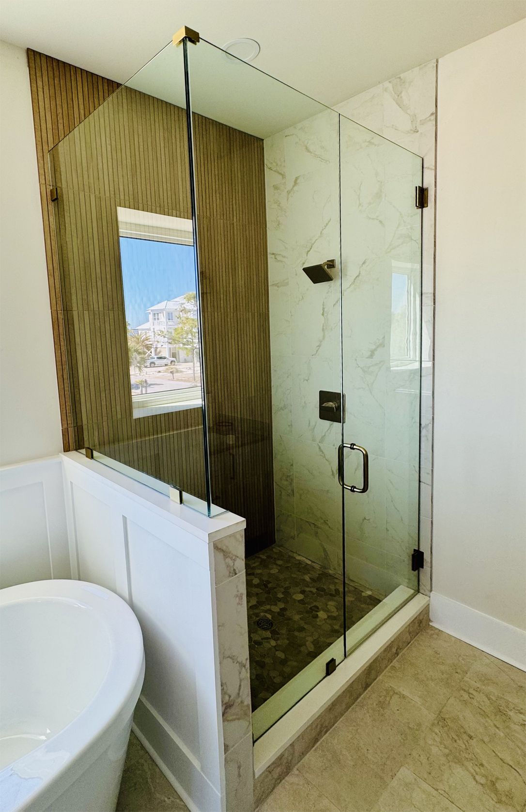 Modern shower with glass door, marble walls, and dark hardware, next to a white tub.