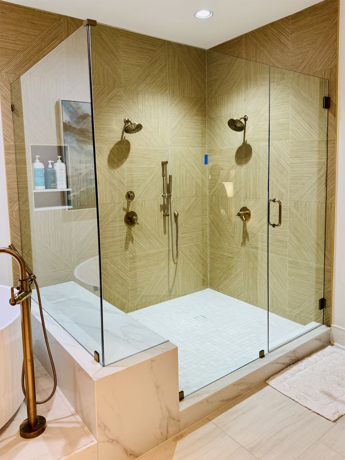 Modern shower with glass doors, multiple shower heads, and white tiled floor and bench.