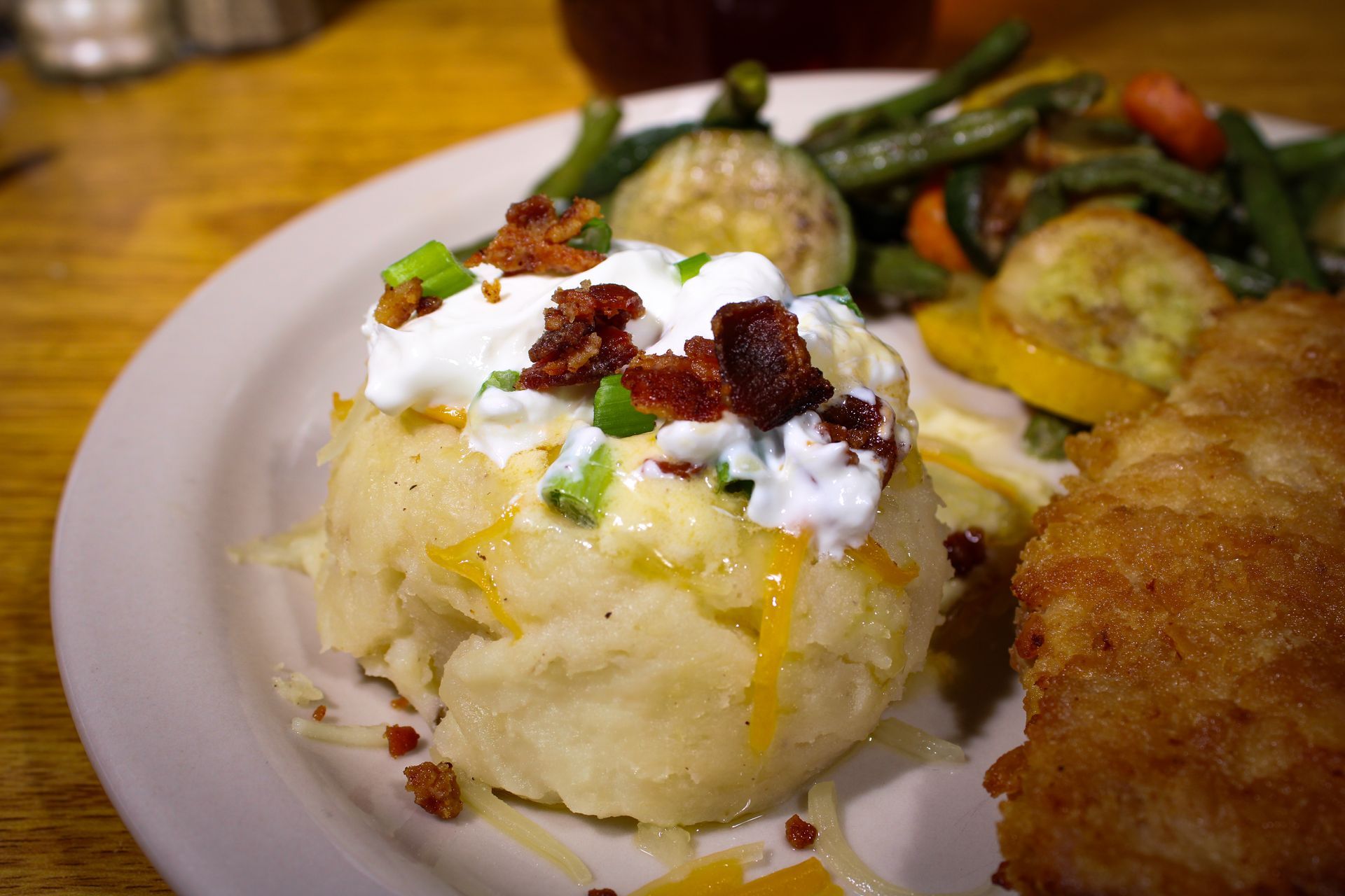 A plate of food with mashed potatoes and vegetables on a wooden table.