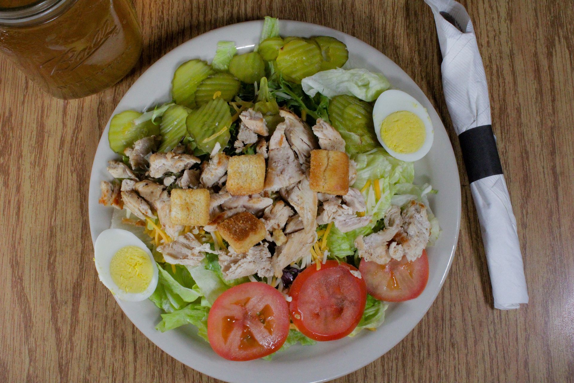 A salad with chicken , eggs , tomatoes and pickles on a plate on a wooden table.