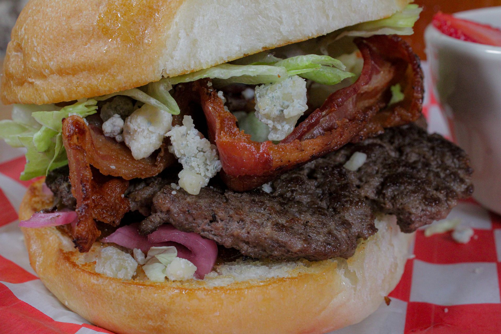 A close up of a hamburger on a checkered napkin on a table.