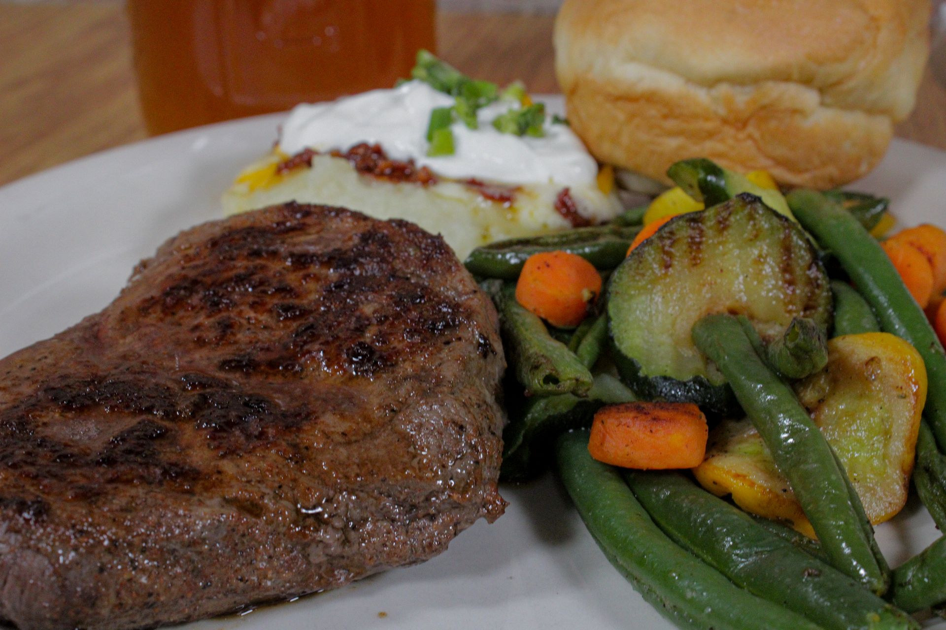 A white plate topped with a steak , green beans , carrots , and mashed potatoes.