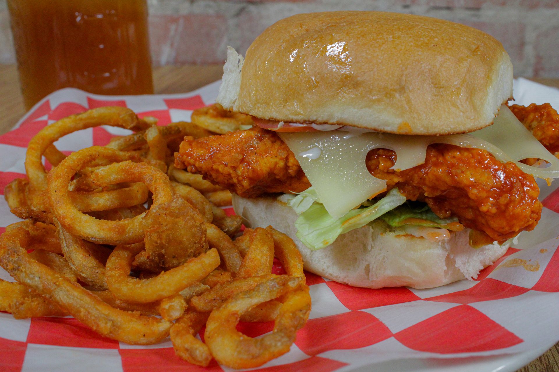 A chicken sandwich with curly fries on a checkered paper on a plate.