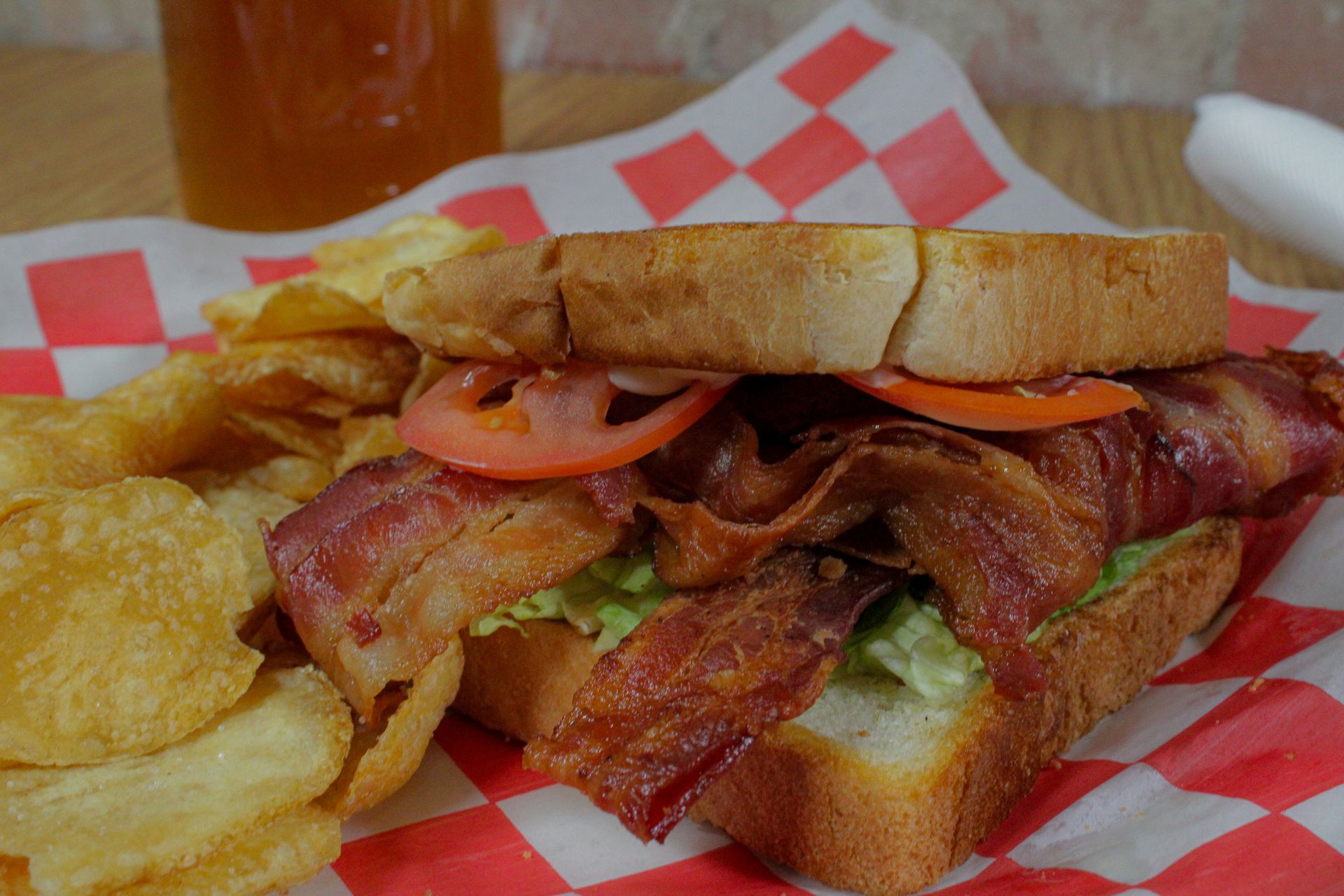 A sandwich with bacon , lettuce , tomatoes and potato chips on a checkered napkin.