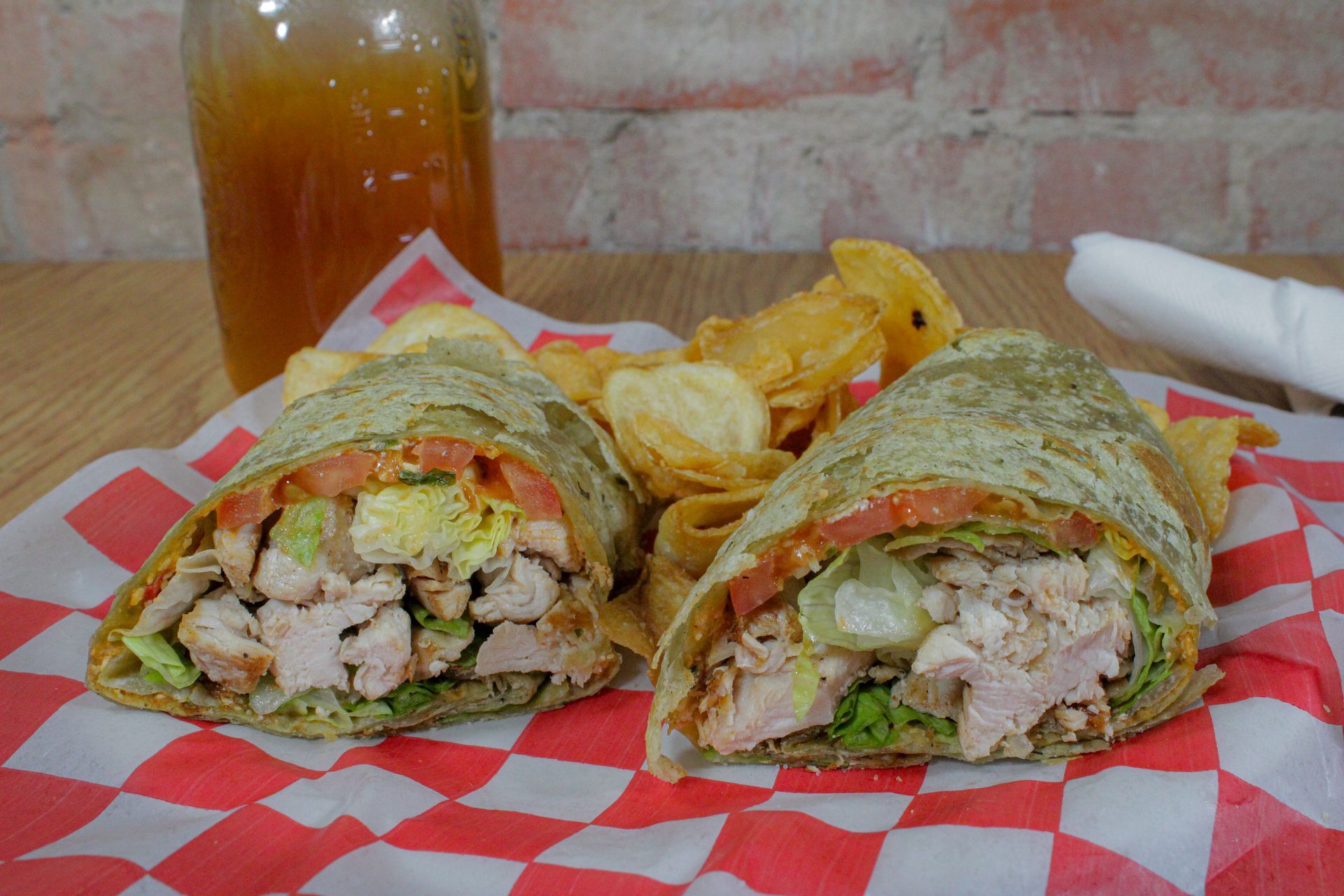 A chicken wrap and chips are on a checkered napkin on a table.