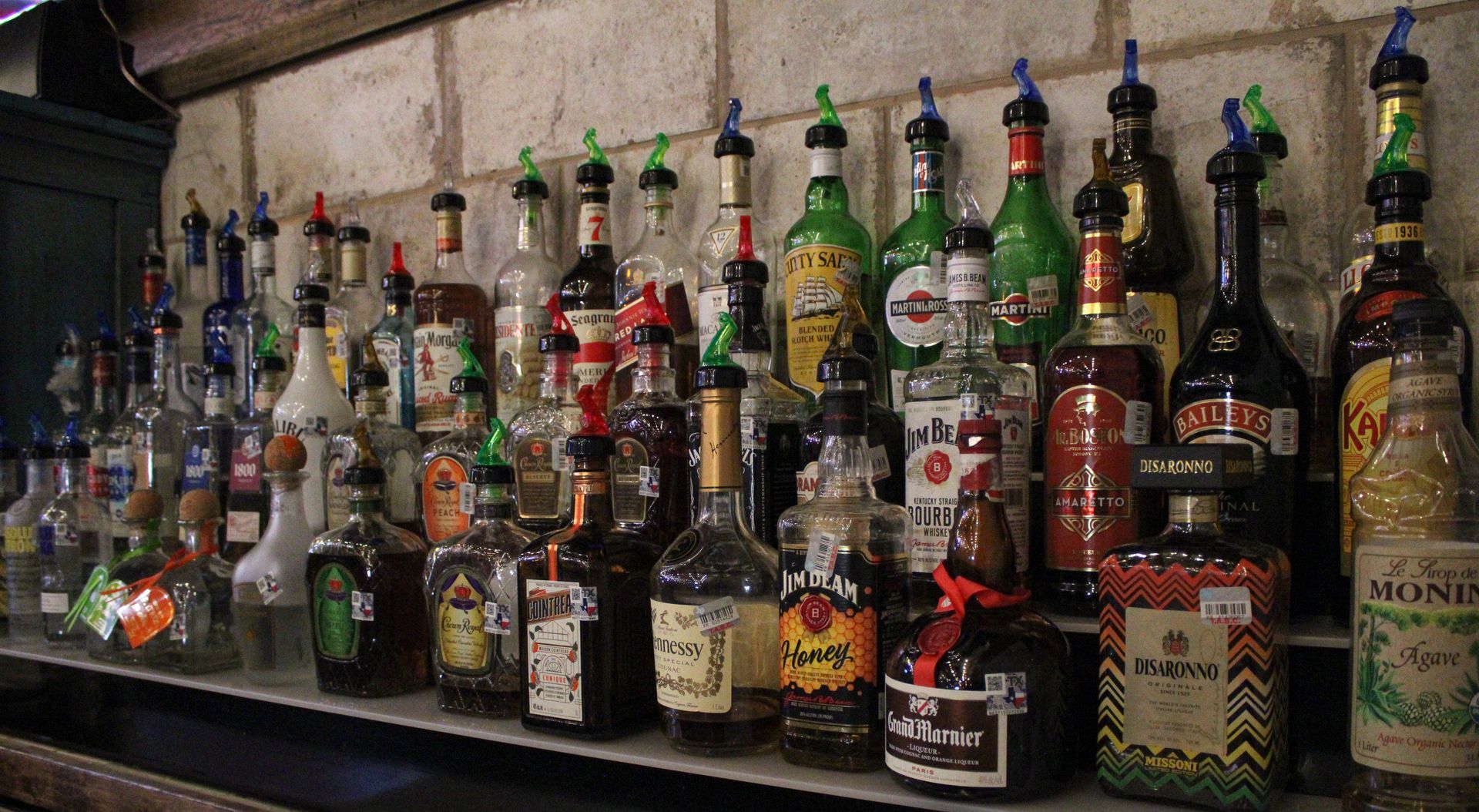 A row of bottles of liquor are lined up on a shelf.