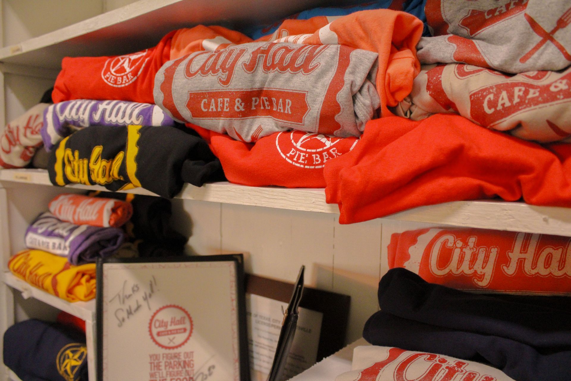 A bunch of shirts on a shelf with one that says city hall
