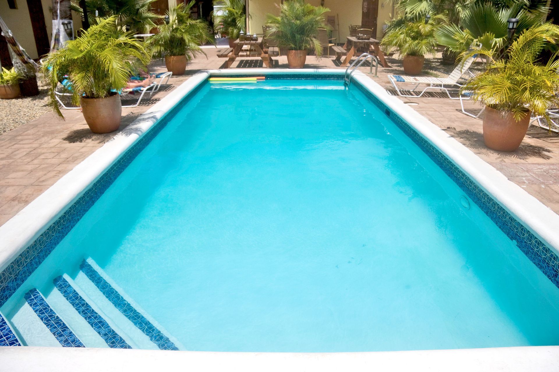 Rectangular swimming pool surrounded by brick patio, potted plants, and lounge chairs.