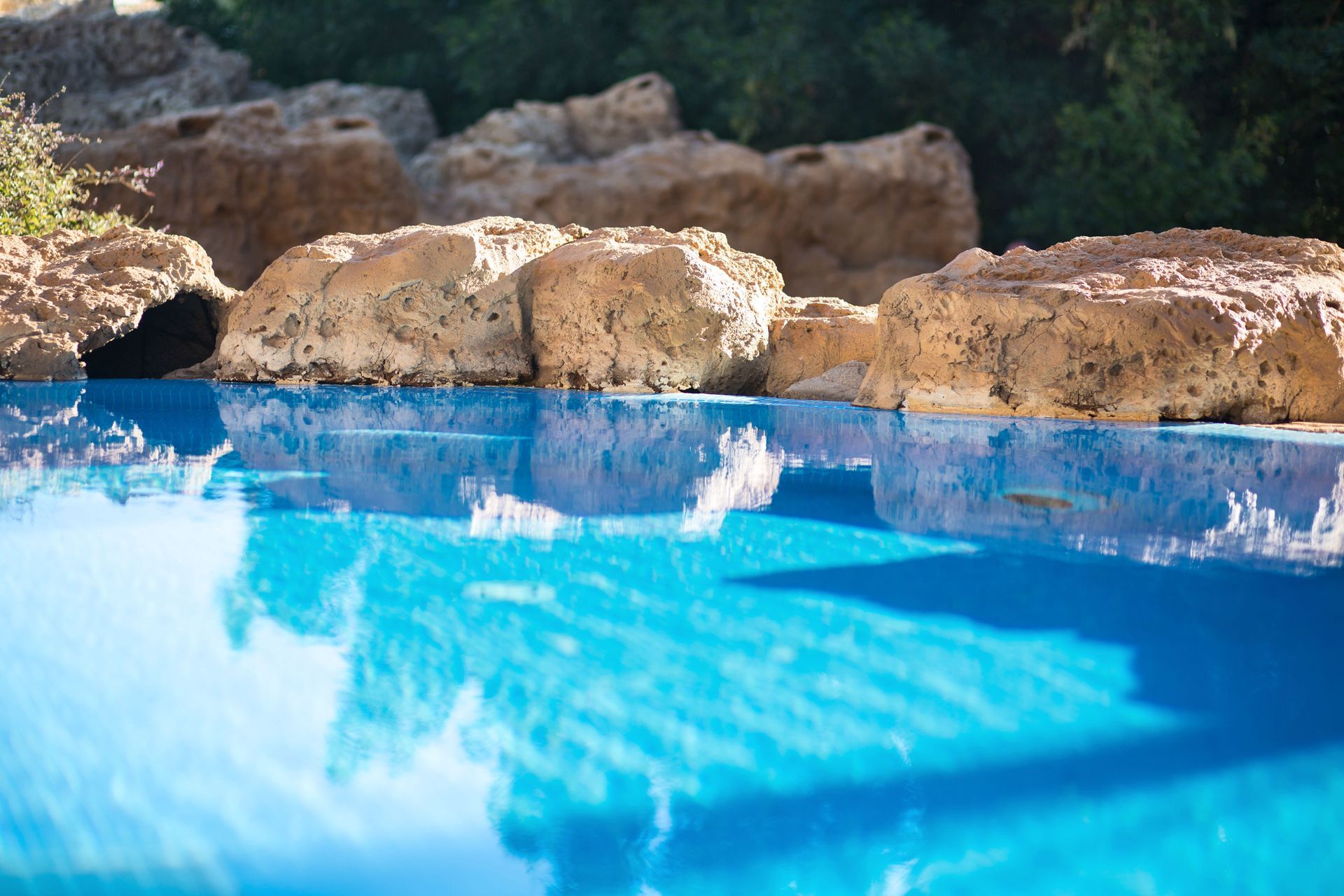 Blue swimming pool with water reflecting the sky, bordered by tan rocks.