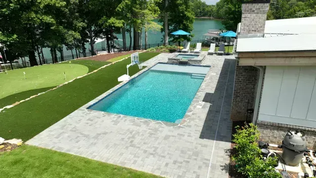 Pool area with pool, spa, putting green, lake view, and lounge chairs.