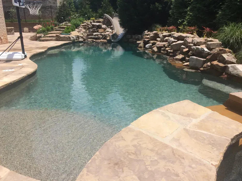 Pool with stone coping, waterfall, and small slide.