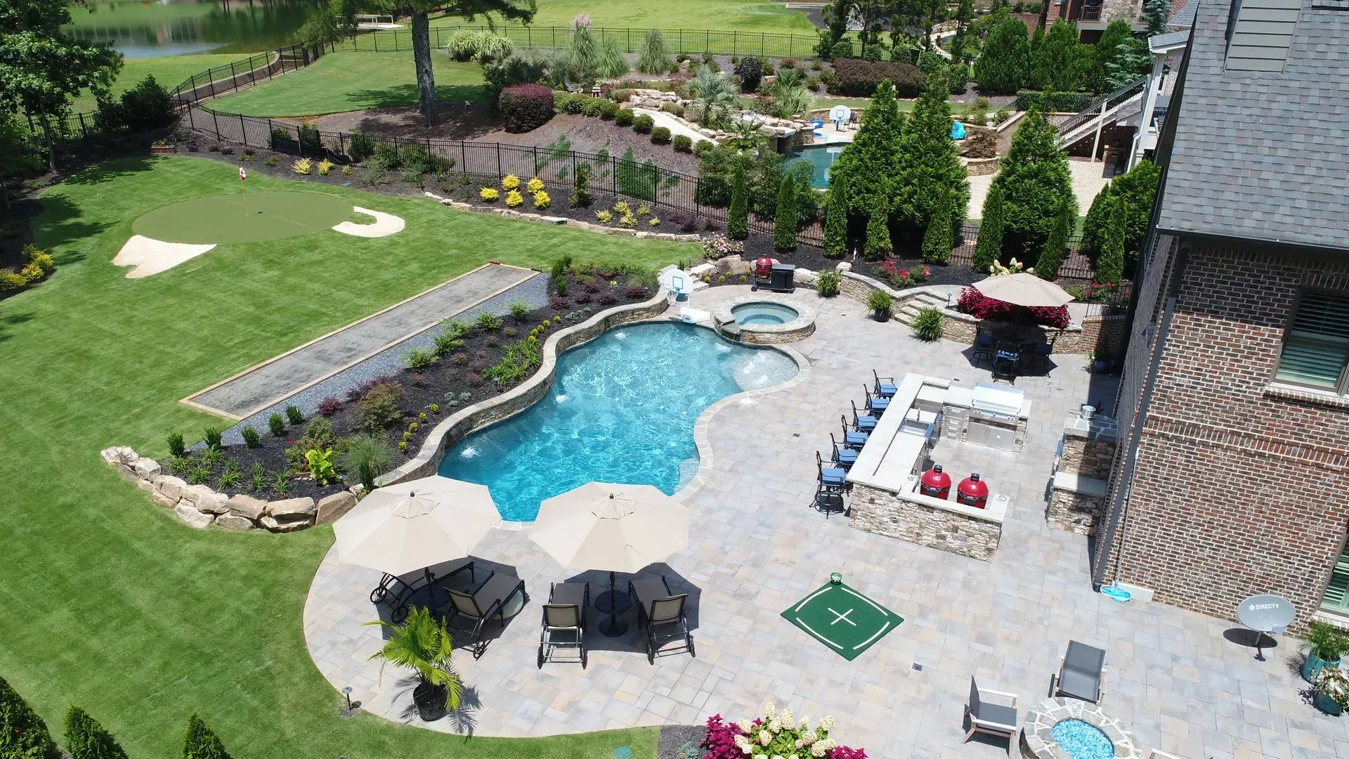Aerial view of a luxurious backyard with pool, patio, bar, putting green, and manicured landscaping.