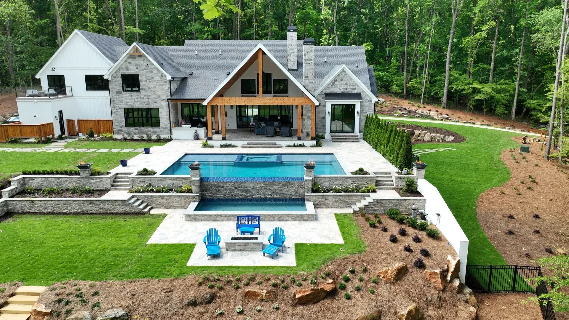 Luxurious home with pool, stone exterior, and lush landscaping in a wooded area.