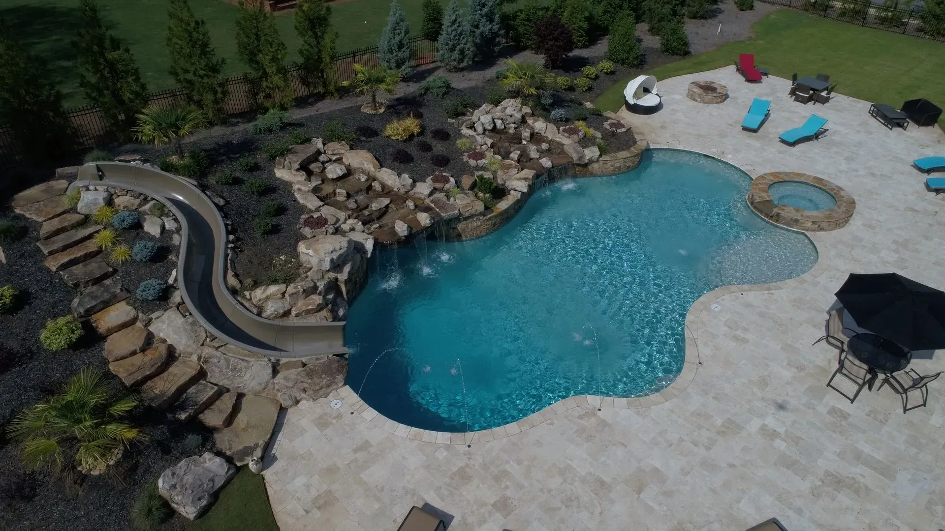 Aerial view of a custom pool with a rock waterfall, slide, and surrounding patio with lounge chairs.
