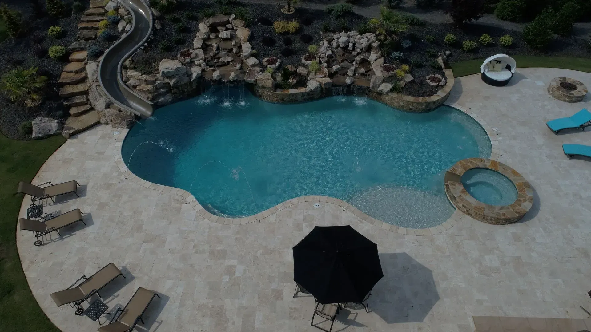 Aerial view of a swimming pool with a slide, waterfalls, a hot tub, and lounge chairs.