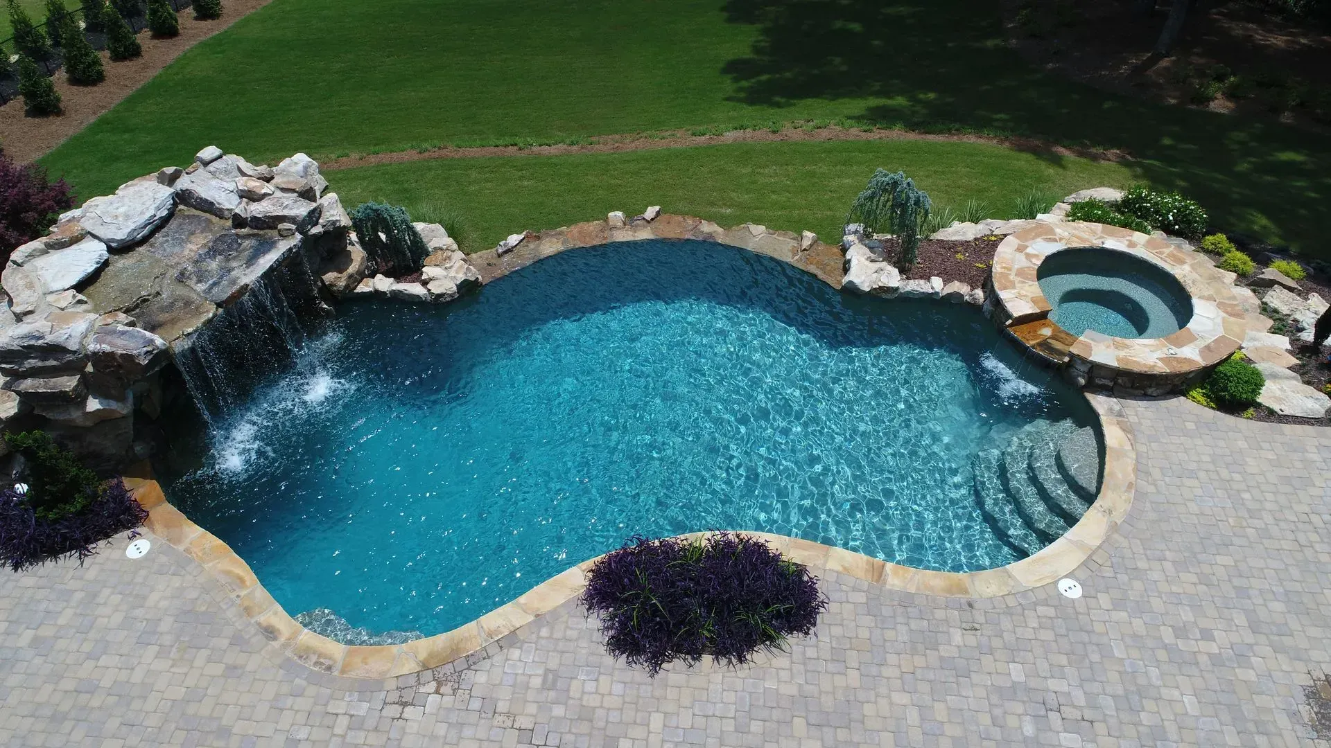 Aerial view of a custom pool with waterfall, spa, and stone edging in a grassy backyard.