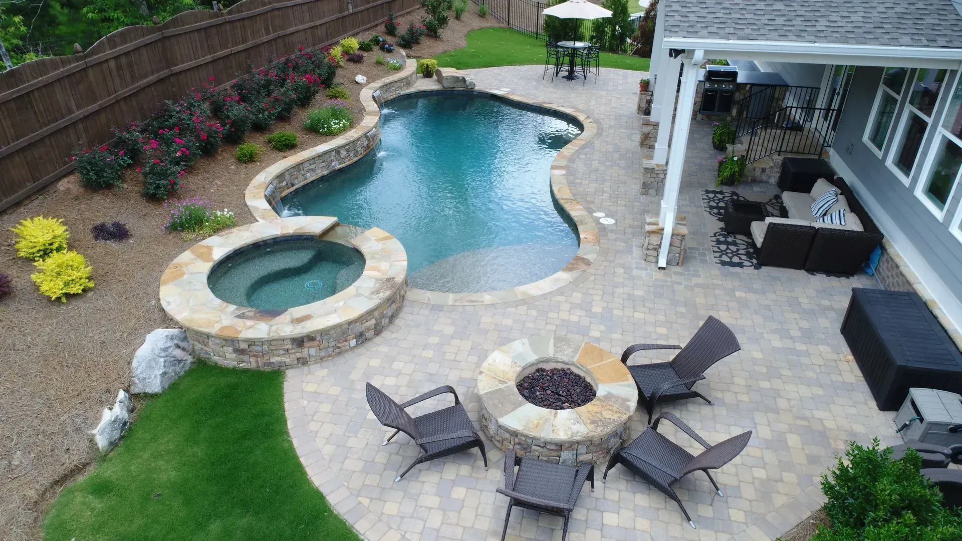 Backyard with pool, hot tub, fire pit, patio, and lush landscaping.