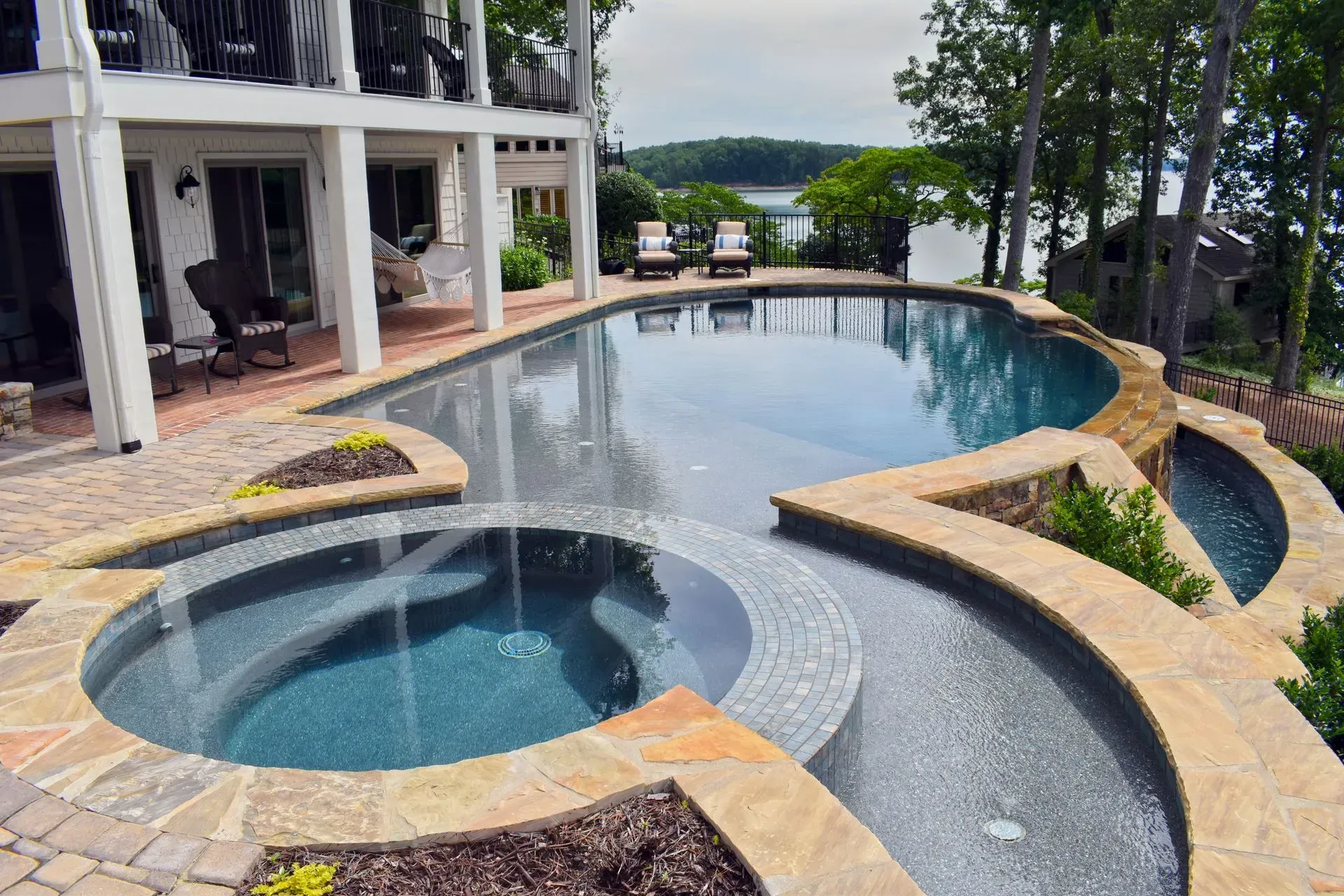 Luxury pool with hot tub, stone walkways, and lake view from a house patio.