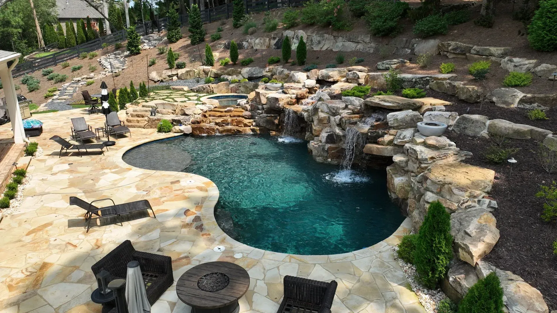 Backyard swimming pool with waterfall, stone deck, and lounge chairs.