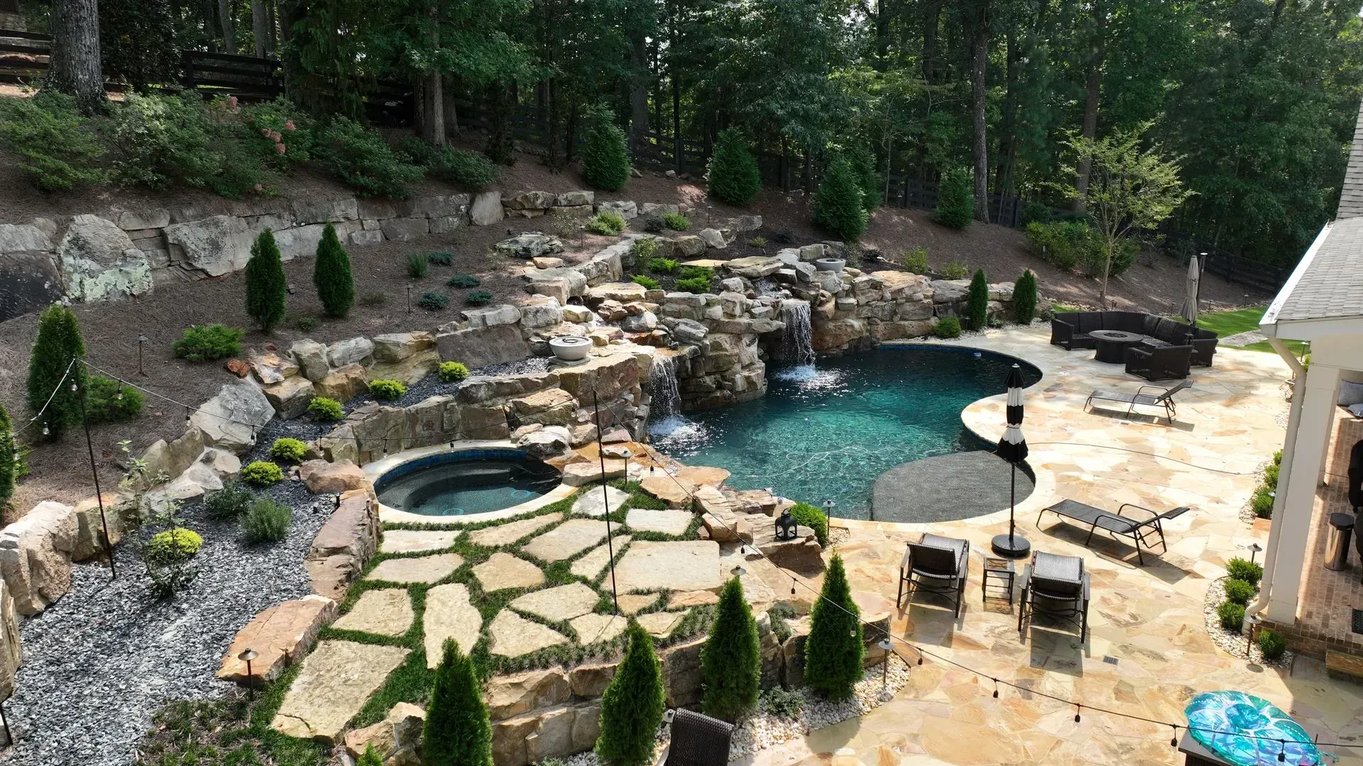 Backyard with pool, waterfall feature, spa, patio, and lush landscaping.