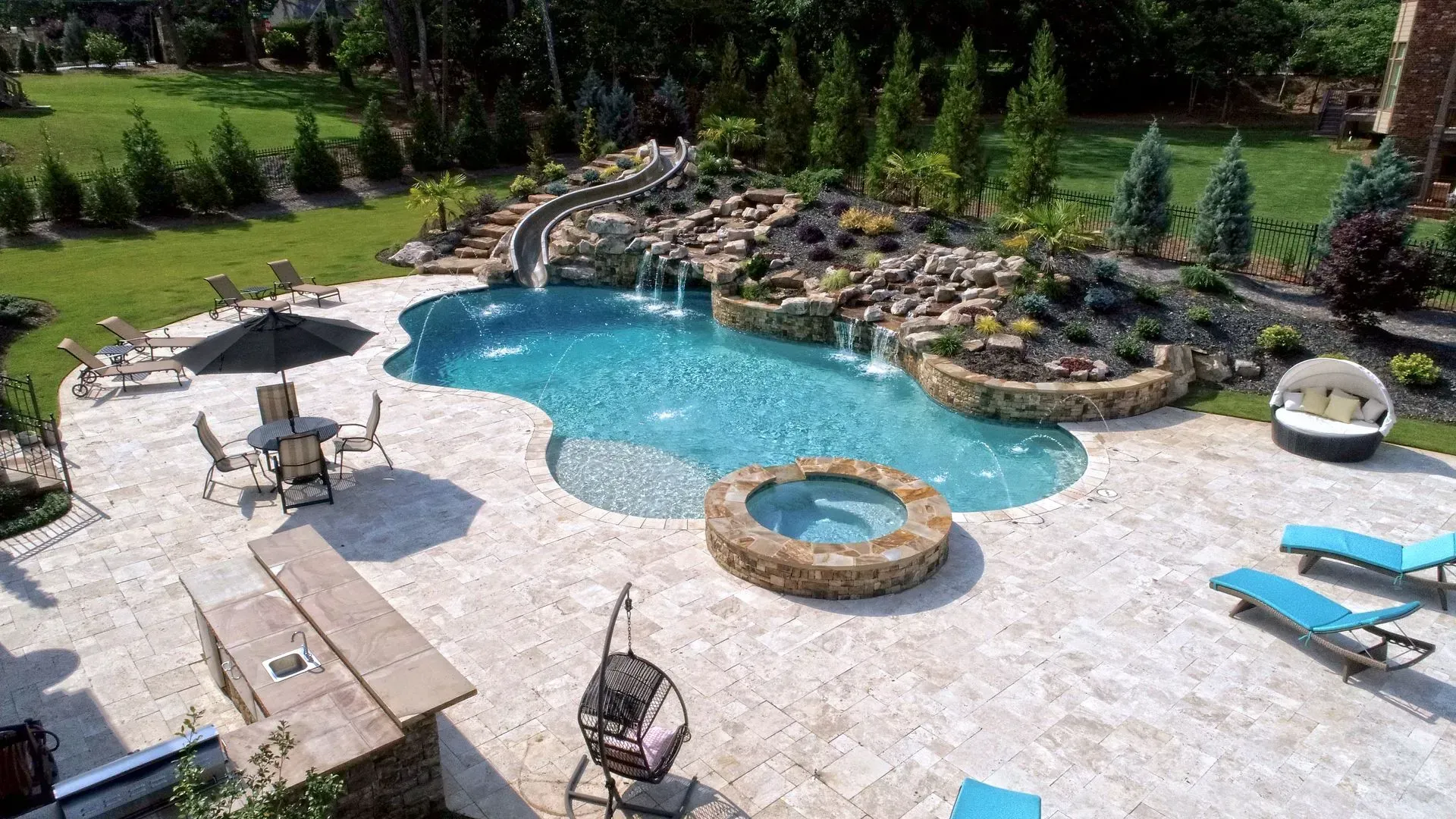 Aerial view of a luxury pool area with waterfalls, slide, spa, lounge chairs, and bar.
