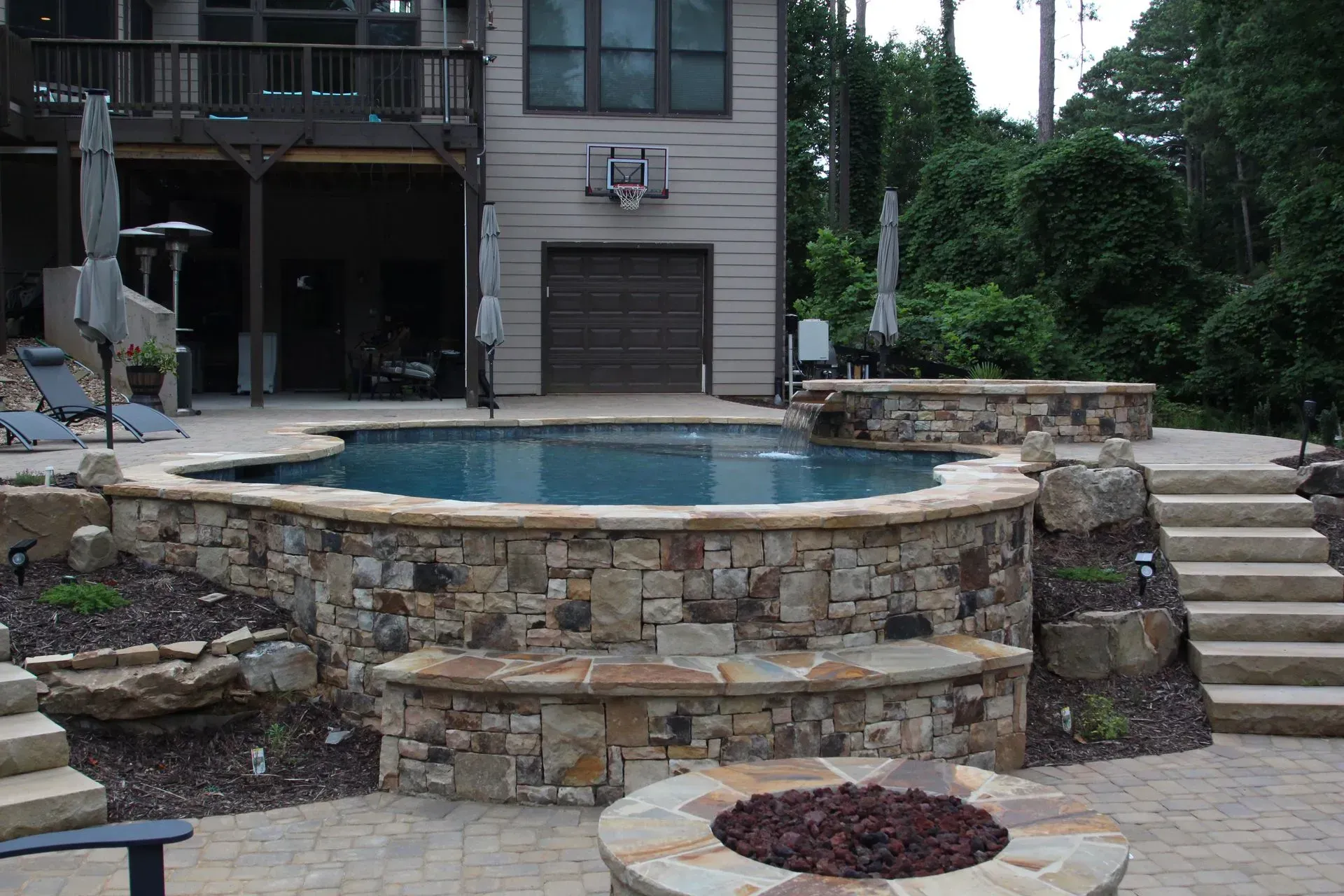 Stone-walled pool area with fire pit, steps, and house in the background.