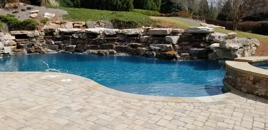 A swimming pool with a stone waterfall feature, surrounded by stone patio.