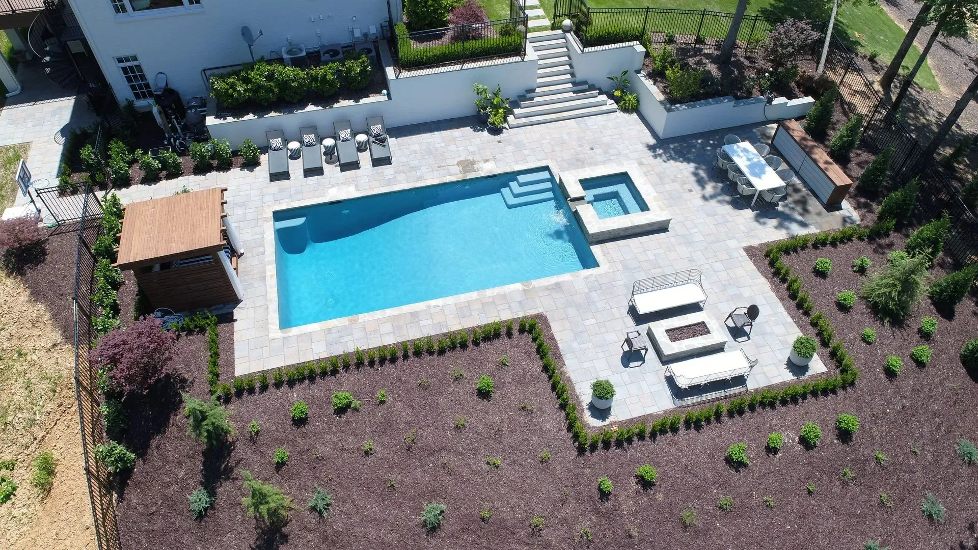 Backyard with pool, hot tub, lounge area, dining table, and landscaping.