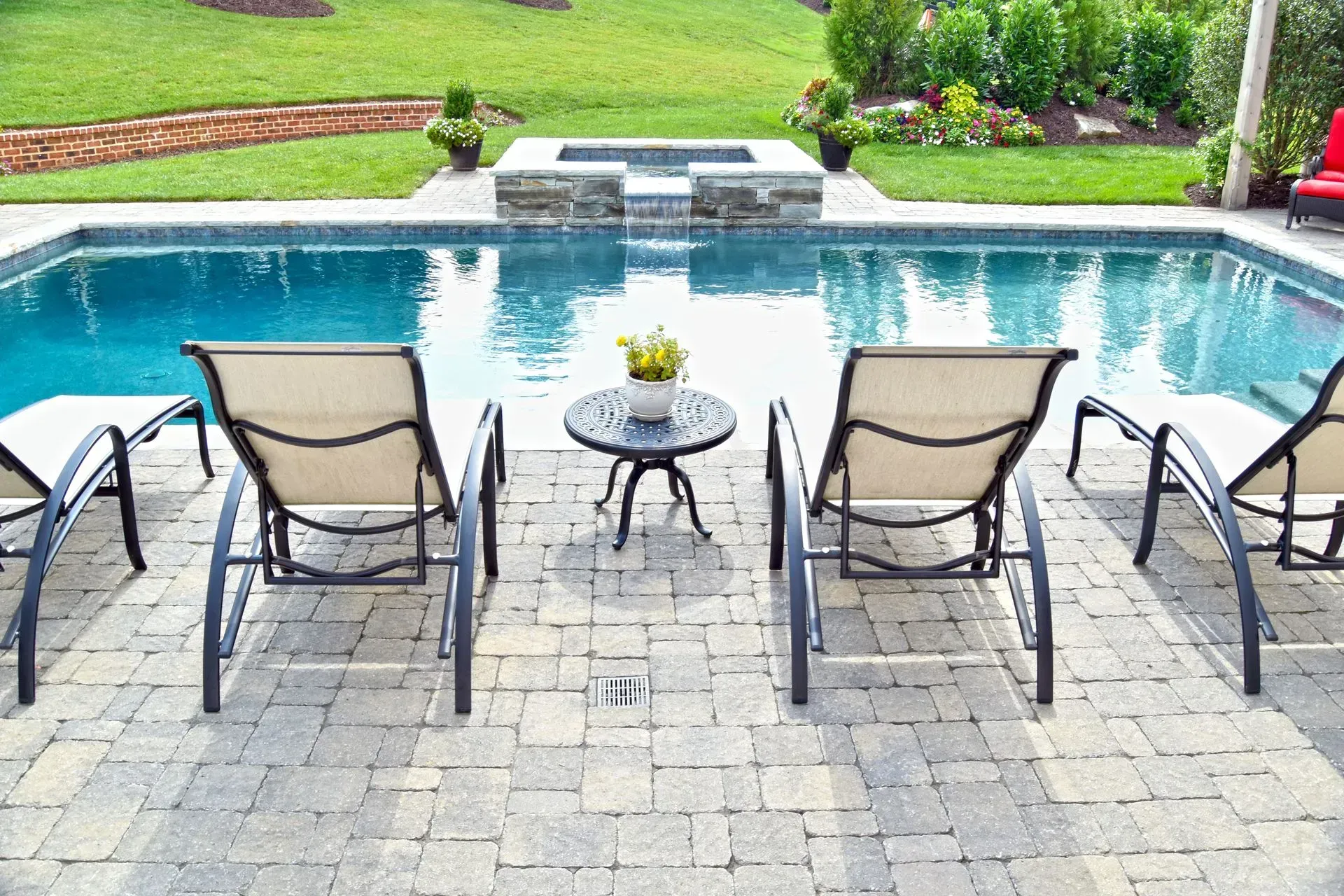 Poolside scene with lounge chairs, small table, and a pool in a backyard.