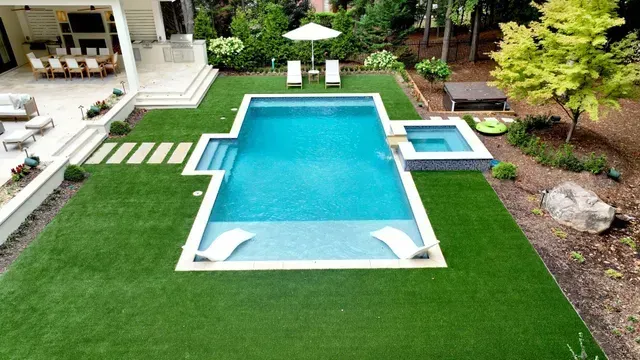 Backyard with pool, hot tub, lounge chairs, green lawn, patio, and lush landscaping.