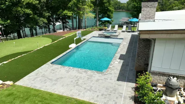 Poolside view with pool, putting green, lake, and seating area.