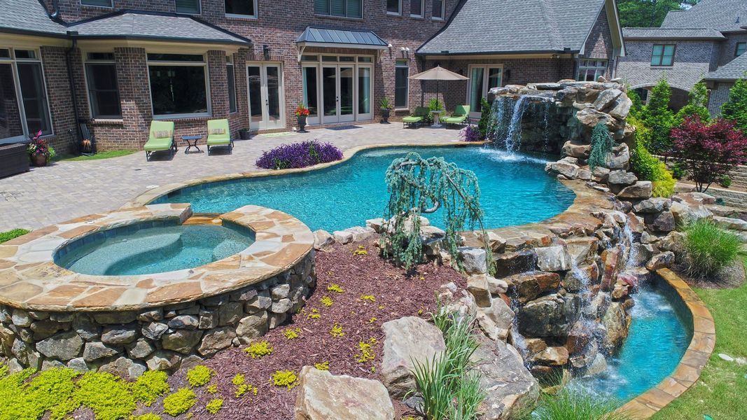 Luxurious backyard pool with waterfall, hot tub, and lush landscaping.