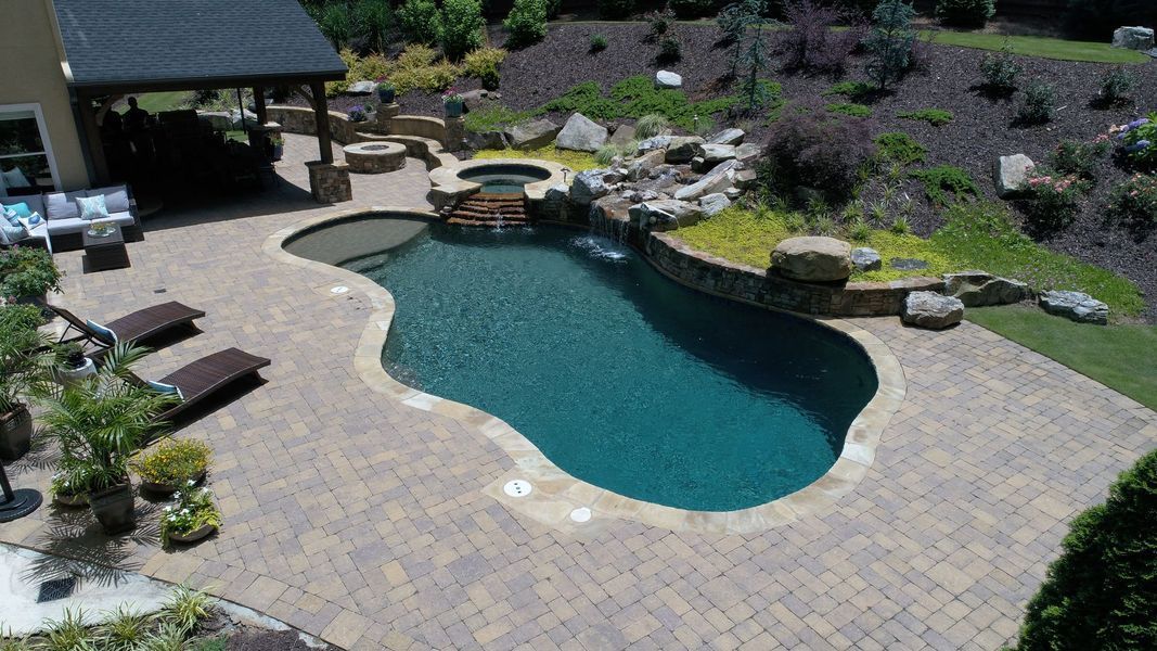 Swimming pool with a waterfall and hot tub, surrounded by stone patio.