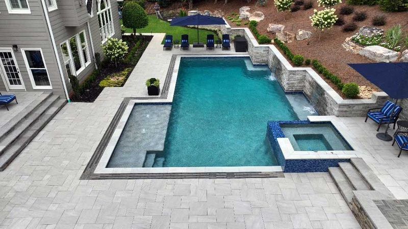Backyard pool with spa, patio, and lounge chairs. Gray stone walls, turquoise water, and blue umbrellas.