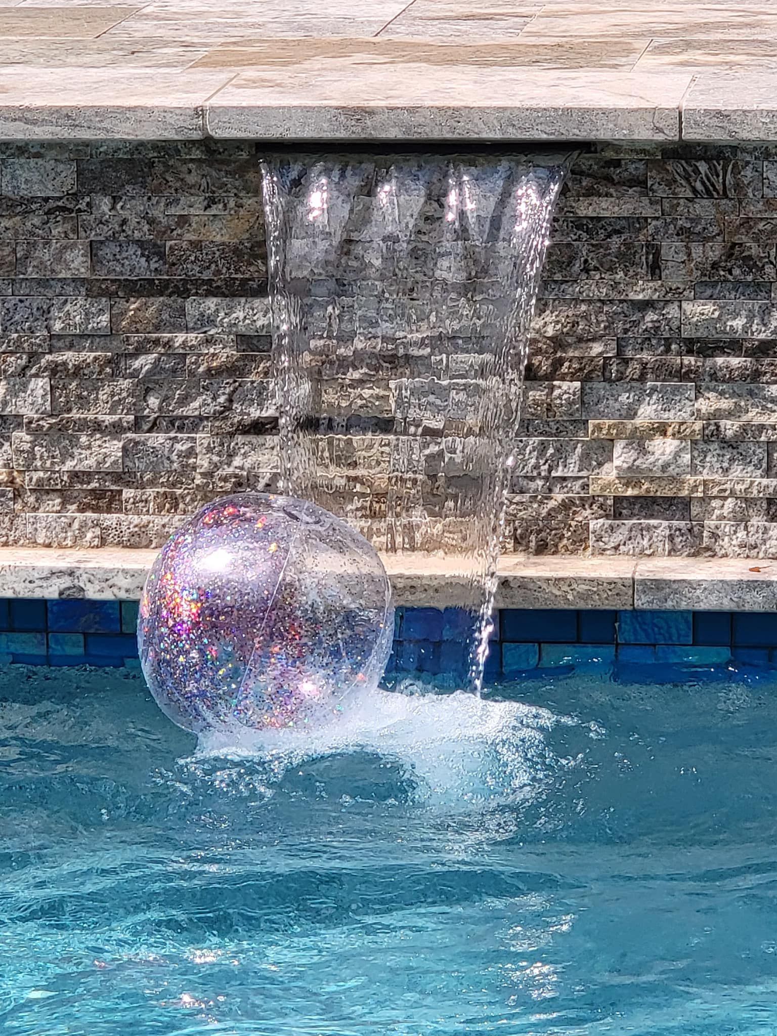 Glittery ball floating in a pool beneath a waterfall.