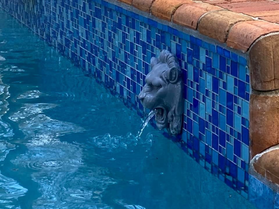 Pool with blue tiles, lion head water fountain, and brick coping.