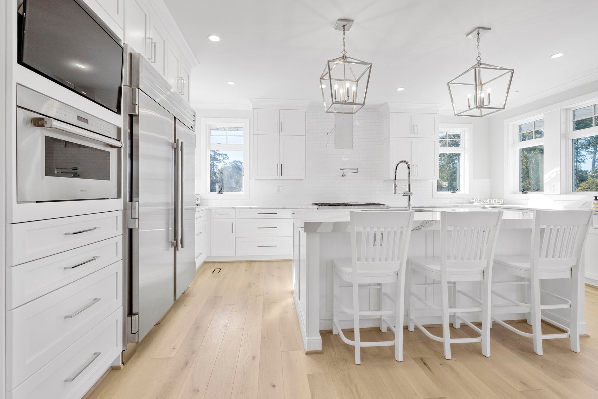 Bright white kitchen with island, barstools, stainless appliances, and light wood floors