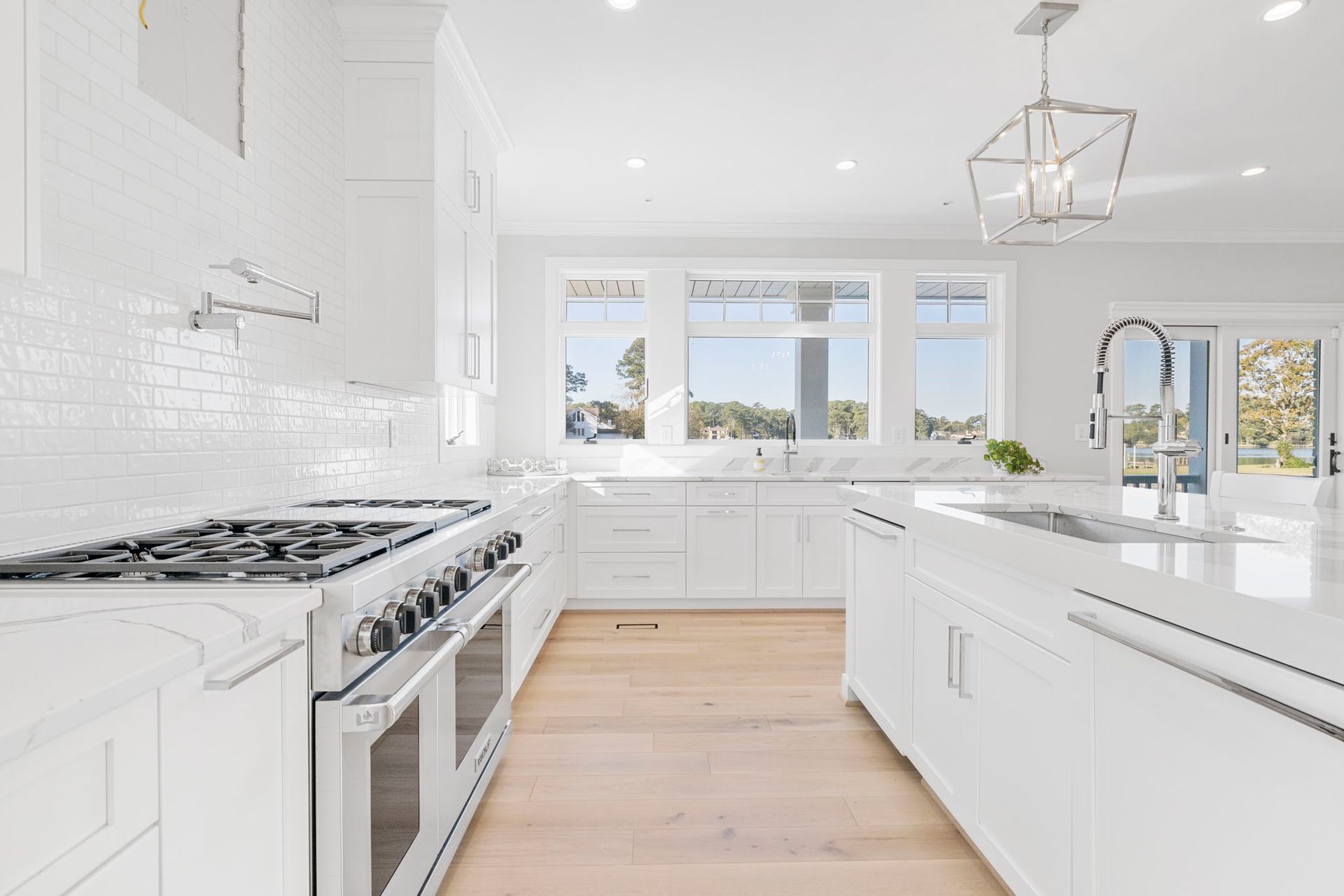 Bright white modern kitchen with gas range, island, hardwood floors, and large windows overlooking greenery
