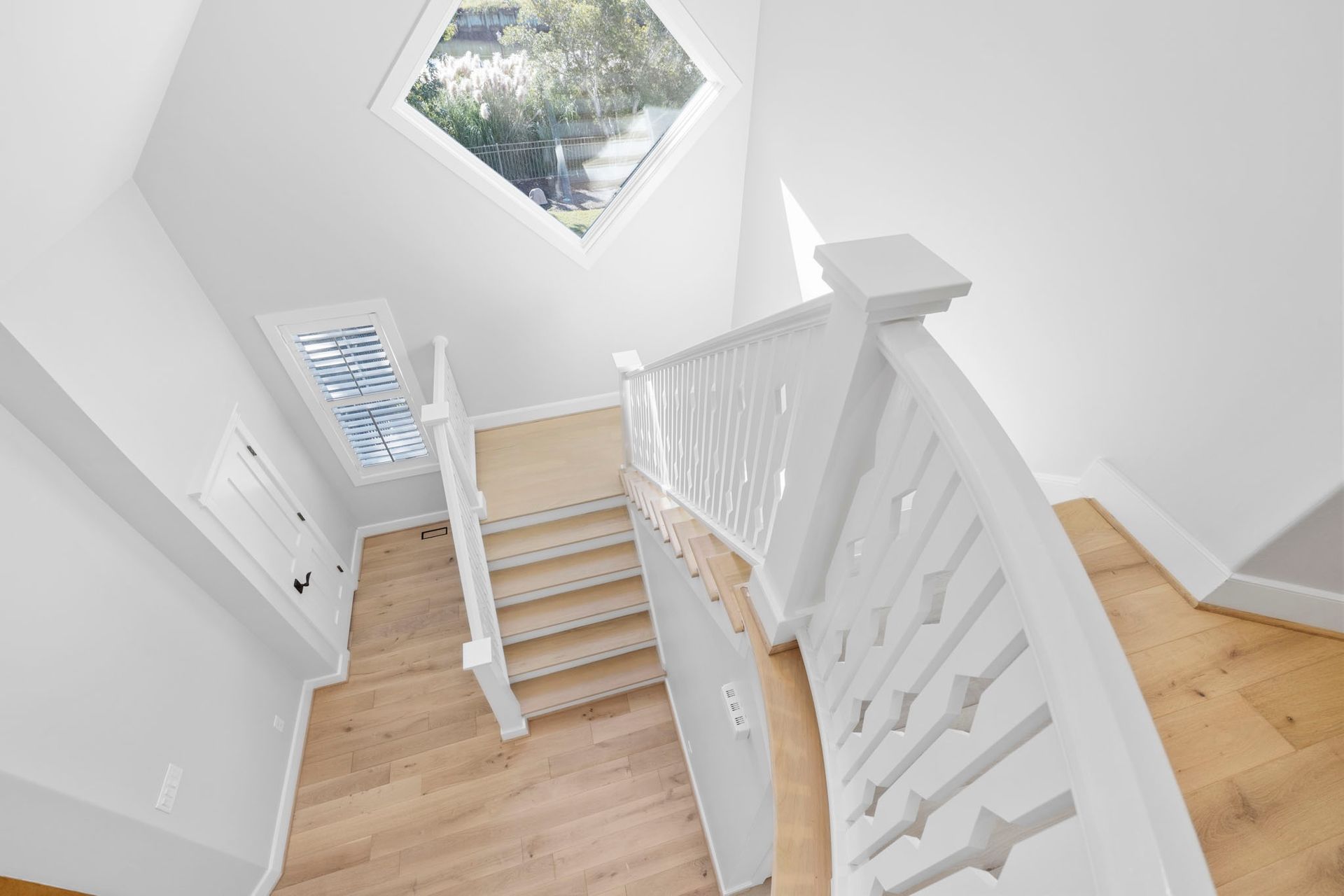 Bright stairwell with white railings, light wood stairs, and a hexagonal window letting in daylight.