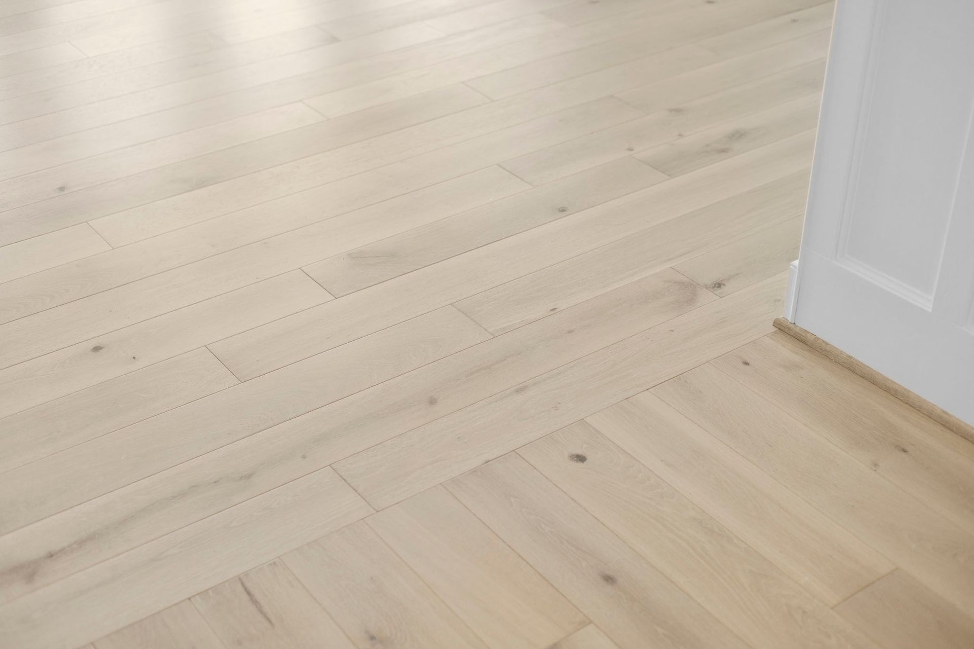 Light wood floor meeting a white wall and doorway in a bright room