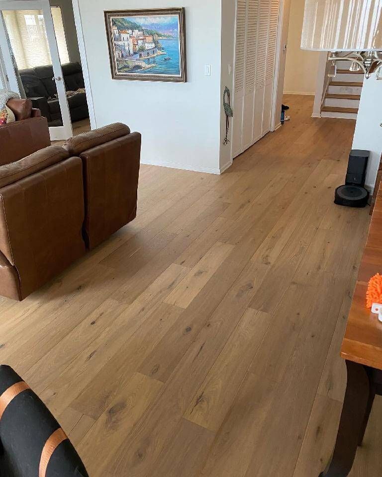 Living room with light wood floors, brown sofa, wall art, and hallway leading to stairs