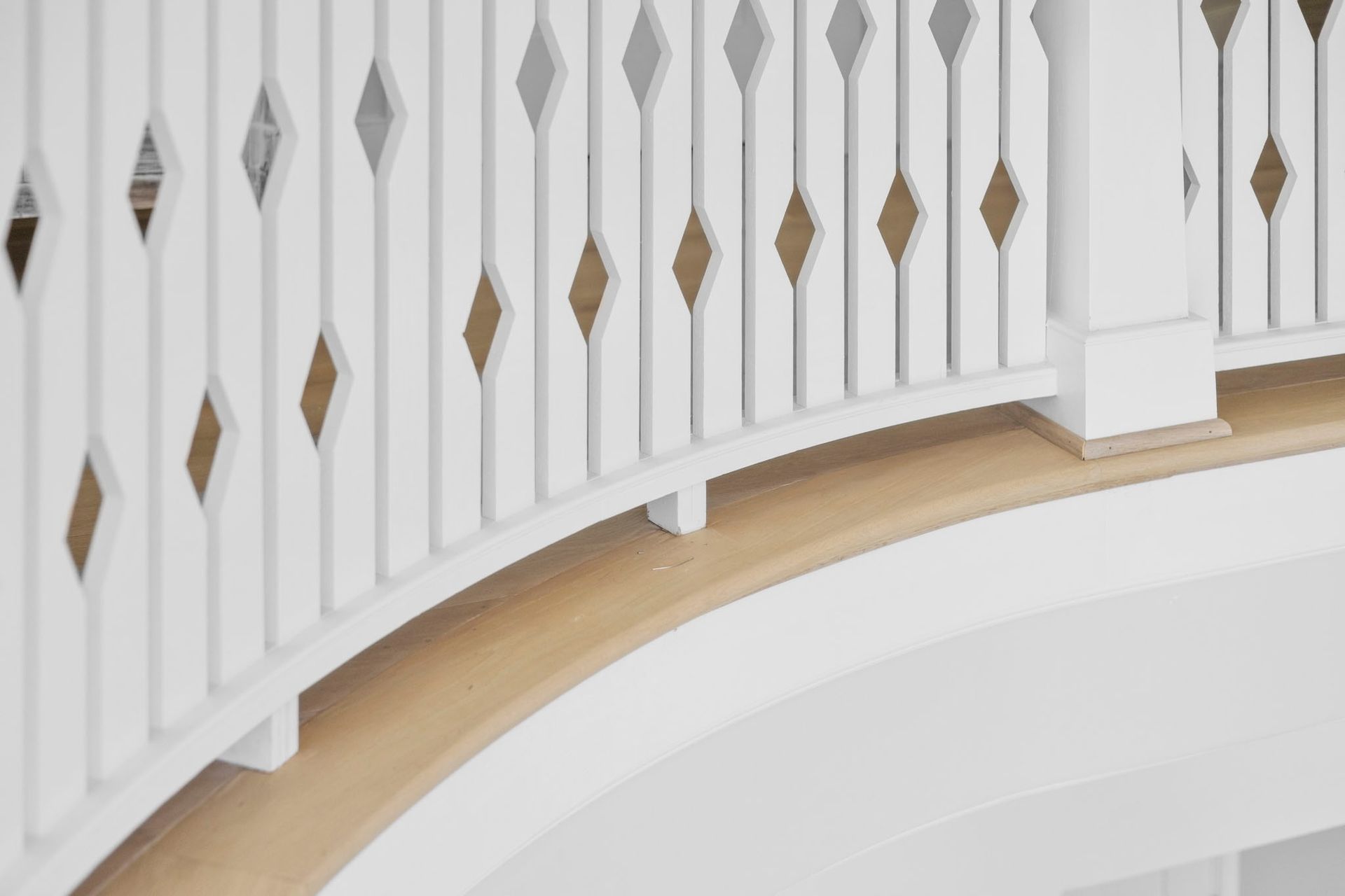 Curved white staircase railing with gold diamond accents over a light wood floor