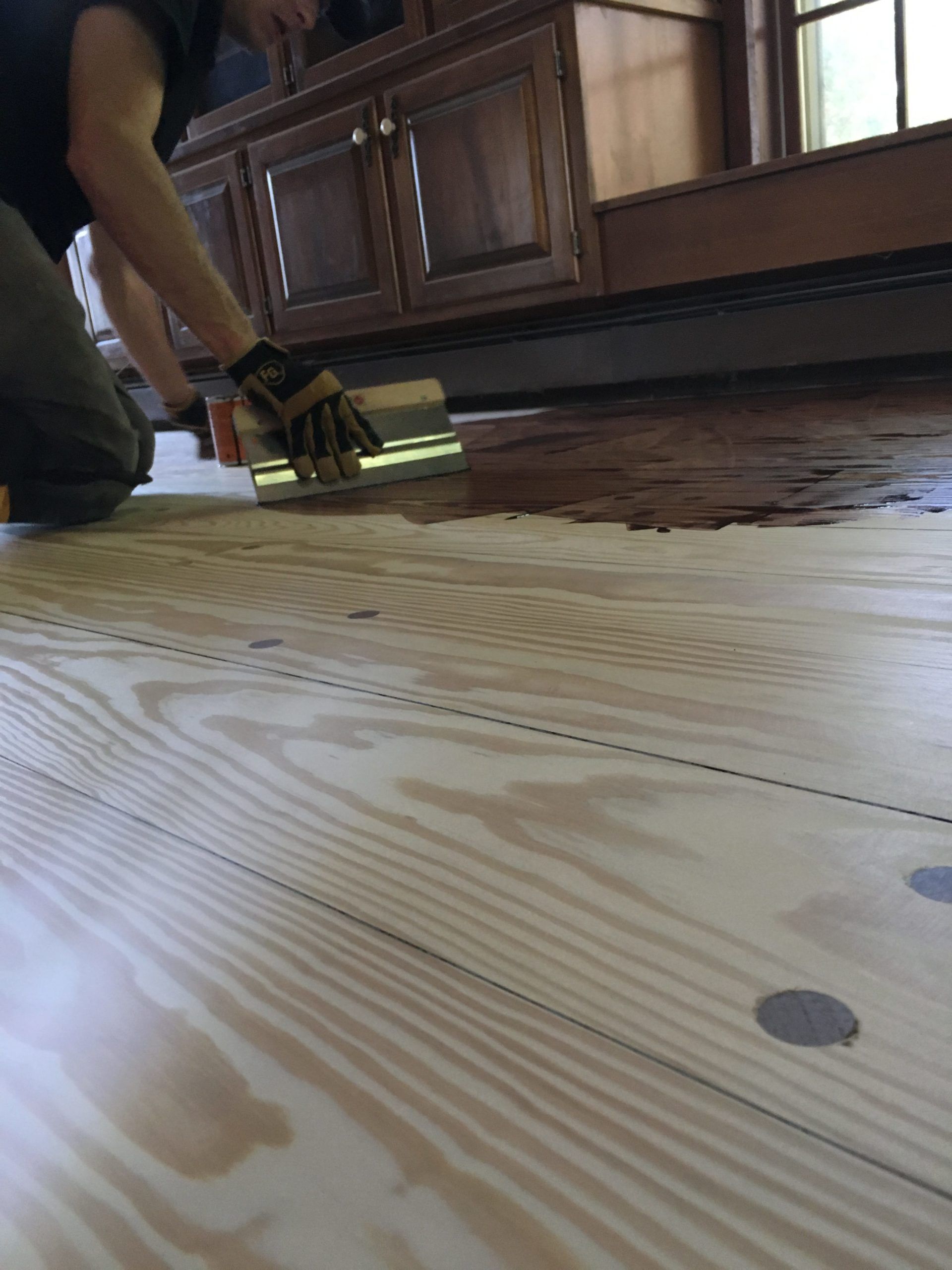 Person using a floor tool on a wooden floor beside dark cabinets