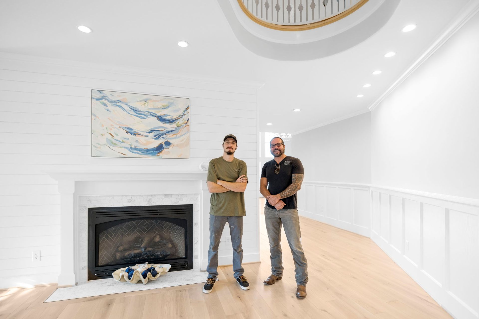 Two men standing in a bright white room with a fireplace and abstract wall art