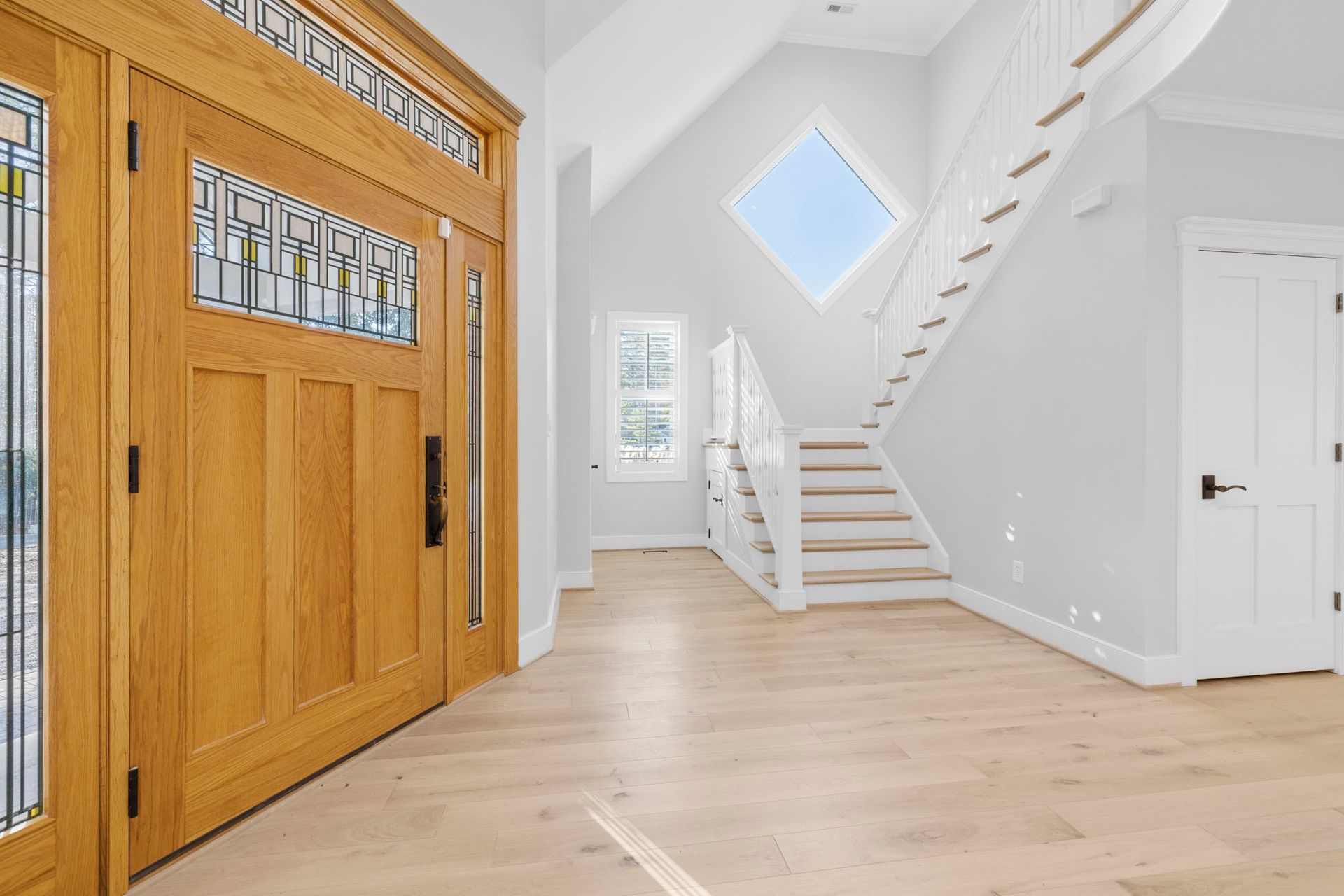 Bright foyer with wood front door, white staircase, light wood floors, and diamond window above the stairs