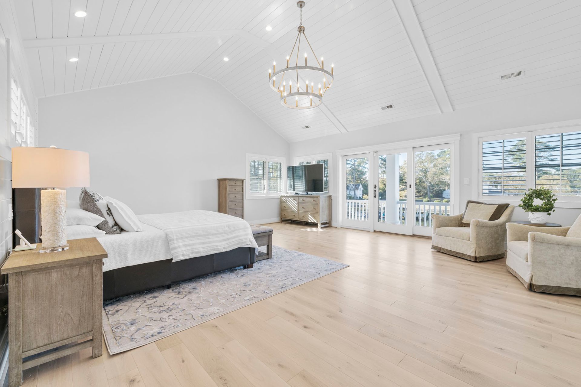Spacious bright bedroom with white bed, chandelier, and large windows overlooking greenery