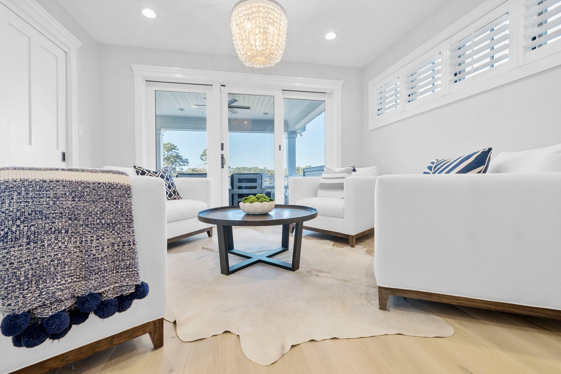 Bright white living room with sofas, coffee table, rug, and large windows opening to a balcony.