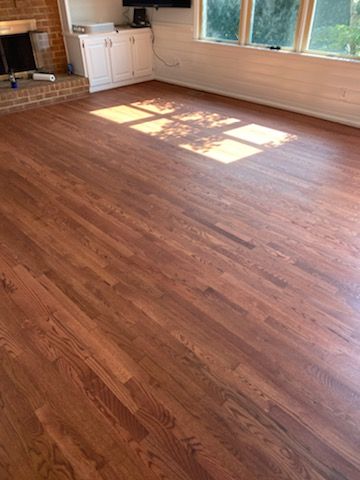 Empty sunlit living room with wood floors, white cabinets, and a brick fireplace