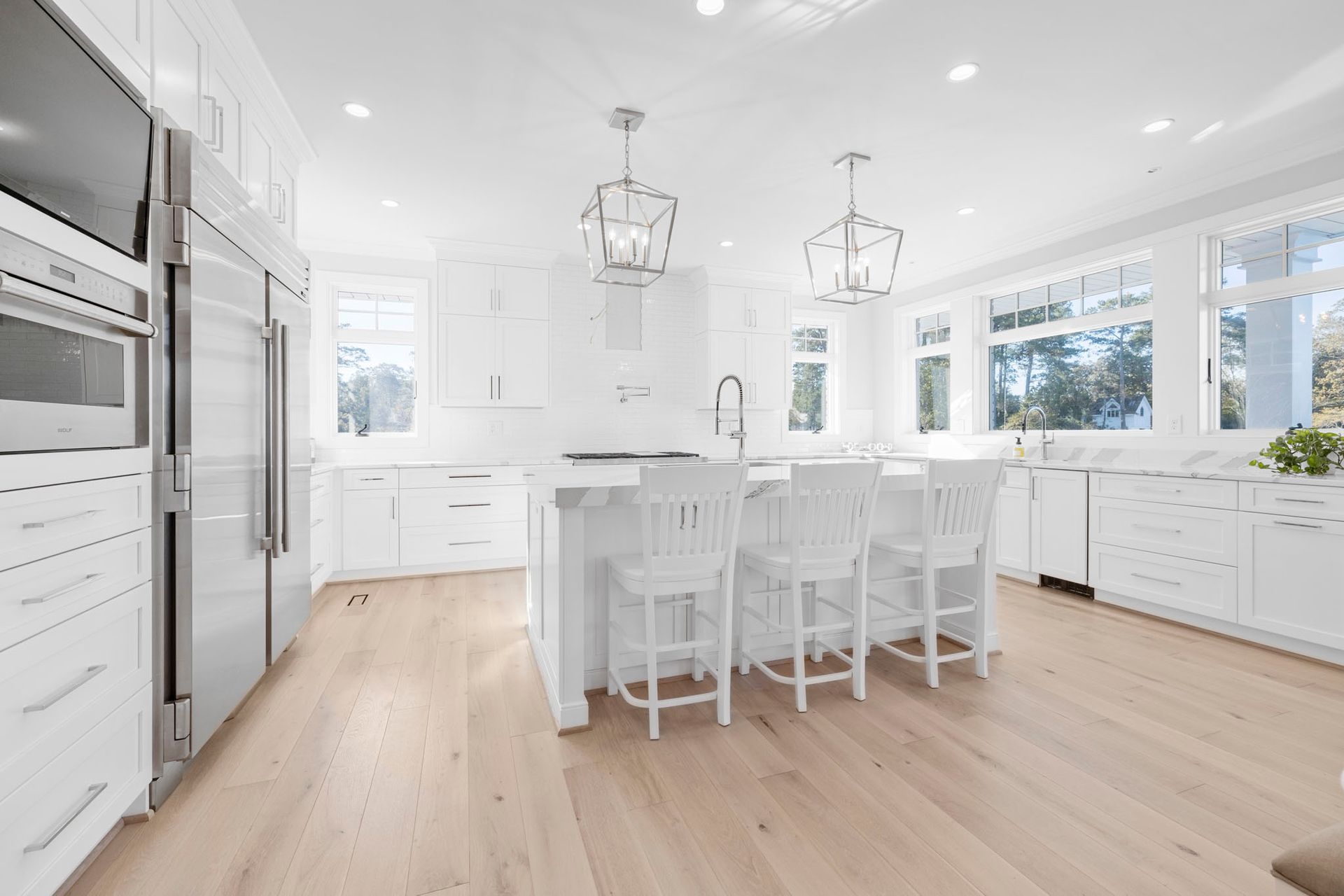 Bright white modern kitchen with island, bar stools, stainless appliances, and light wood floors
